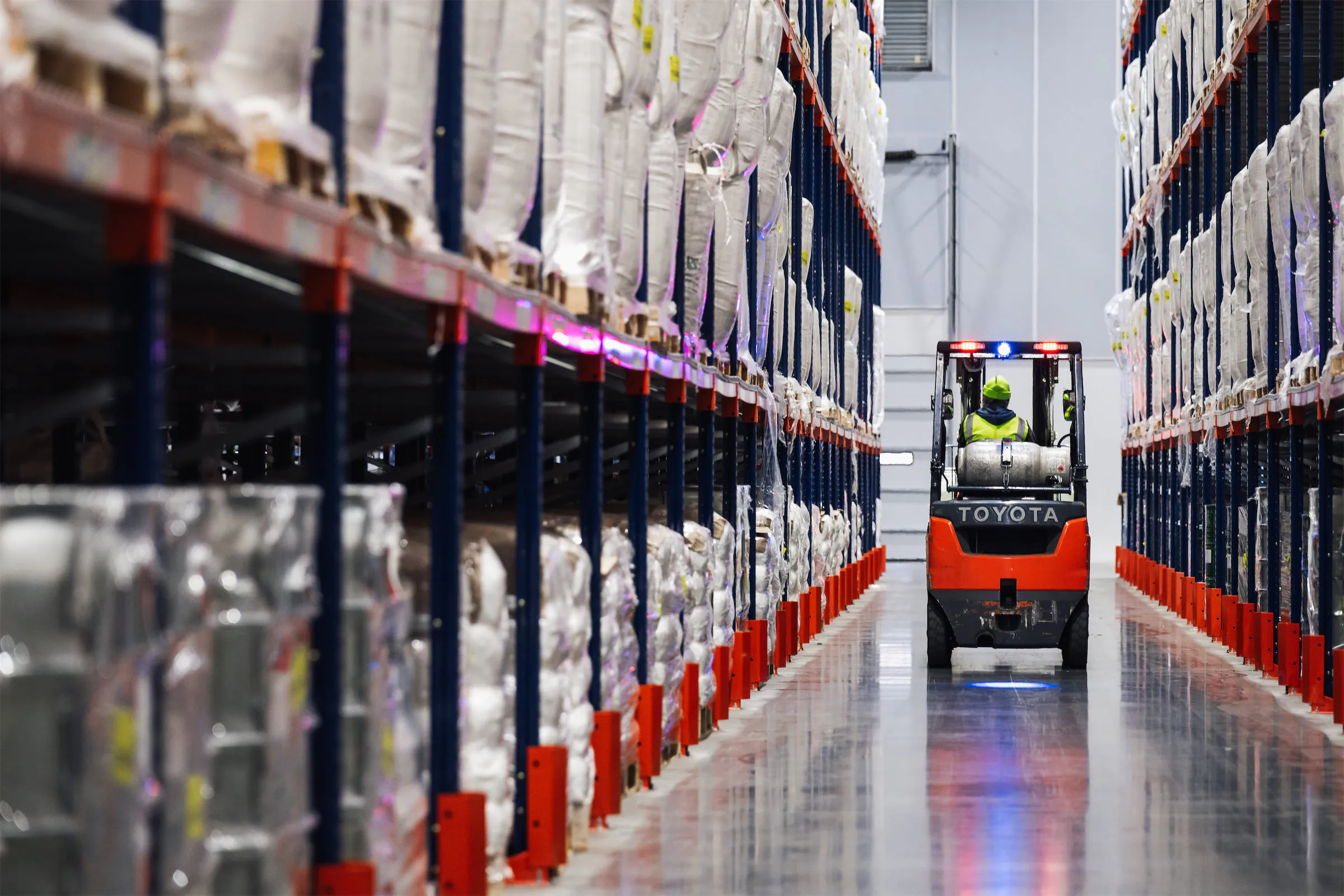 Forklift driving down a warehouse aisle lined with pallet racks